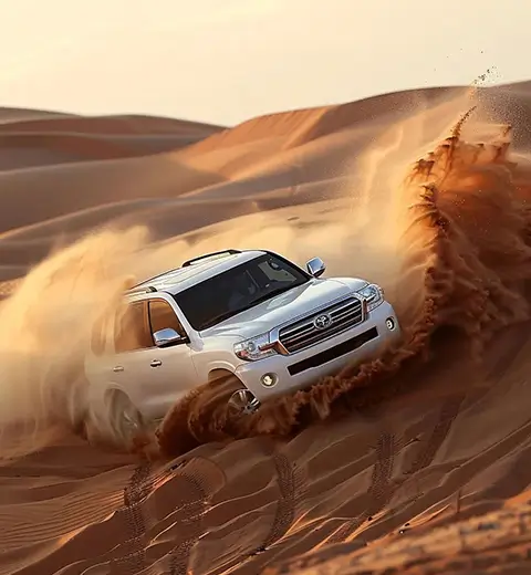 A white Toyota Land Cruiser powerfully driving through the sand dunes, kicking up sand during a thrilling dune bashing experience in the Dubai desert.