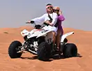 A couple wearing traditional attire enjoys quad biking in the desert landscape.