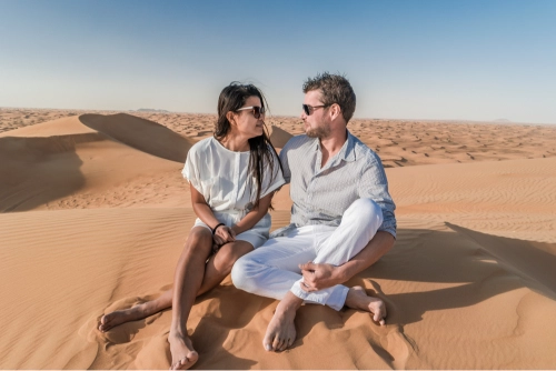 Couple relaxing on sand dunes during a romantic Desert Safari in Dubai, enjoying the scenic beauty of the Arabian desert – ideal for booking Dubai Desert Safari tickets for couples.